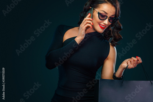 Shopping on Black Friday and Cyber Monday. Sale concept for shops. Woman holding bag and calling on the phone , isolated on dark background