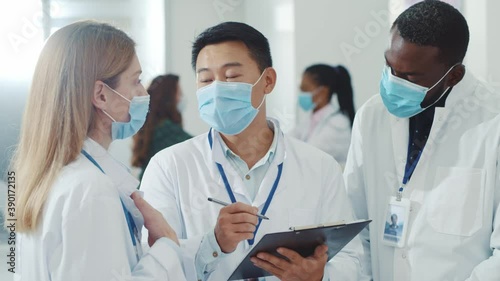 Diverse female and male doctors discussing treatment creating medicl report negotiating taolking wearing face masks for virus protection. Healthcare. Quarantine. Hospital during pandemic. photo