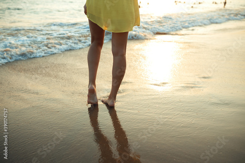 A young girl walks on the seashore in the rays of the setting sun A girl is dressed in a yellow sundress © toxicoz