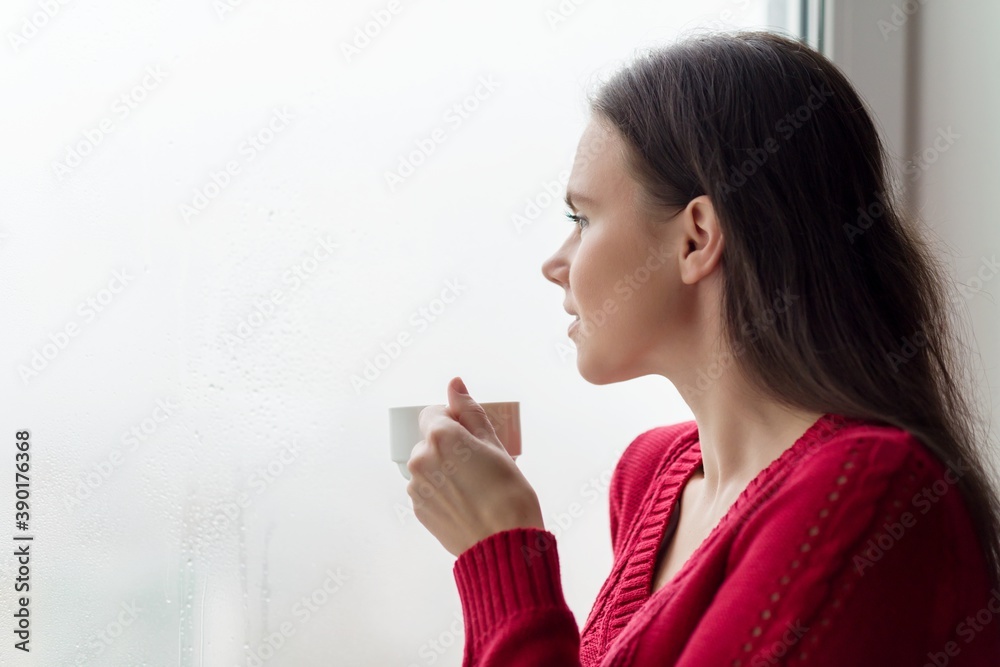 Young smiling woman enjoying coffee, female in warm knitted sweater near the window Young smiling woman enjoying coffee, female in warm knitted sweater near the window