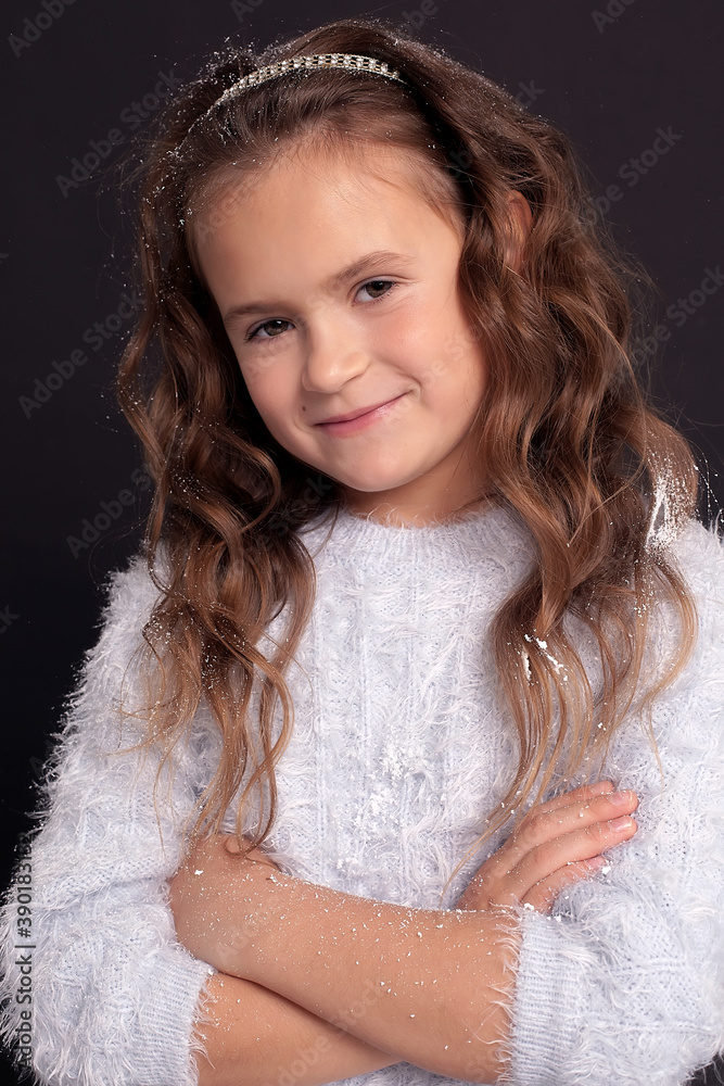 A beautiful little girl of European appearance with long blonde hair in a Christmas dress poses for a photo A beautiful little girl of European appearance with long blonde hair in a Christmas dress poses for a photo