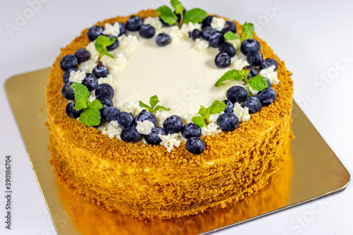 Honey cake with blueberries and leaves of mint on golden plate. Homemade honey cake with sour cream on a white table.
