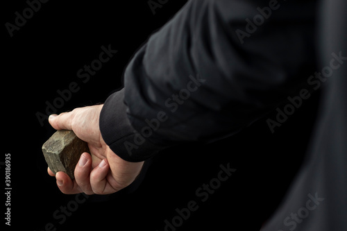 Cobblestone in male hand on black background. Riot concept.