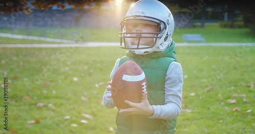 Cheerful happy child in helmet playing American football outdoors in sunny day at public park. Family sports weekend. 4K video.
