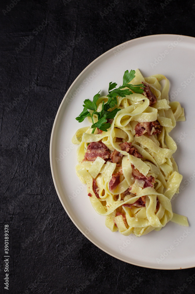 Traditional Italian pasta dish, spaghetti carbonara with parmesan cheese, bacon in white plate on black background, top view. Italian dinner with pasta