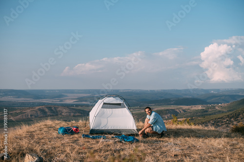 Young male tourist puts a tent in the mountains.