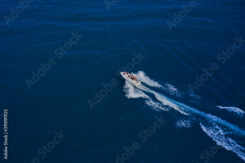 Drone view of a boat sailing across the blue clear waters. Top view of a white boat sailing in the blue sea.  Aerial view luxury motor boat. White boat with people.