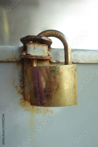 Close up rusty golden iron pad lock. Grey wall in background