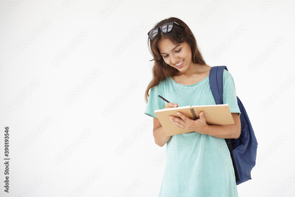 Attractive cute female student of mixed race appearance carrying backpack and writing down her thoughts in personal diary. Pretty teenage girl with bag doing homework, making notes in copybook Attractive cute female student of mixed race appearance carrying backpack and writing down her thoughts in personal diary. Pretty teenage girl with bag doing homework, making notes in copybook