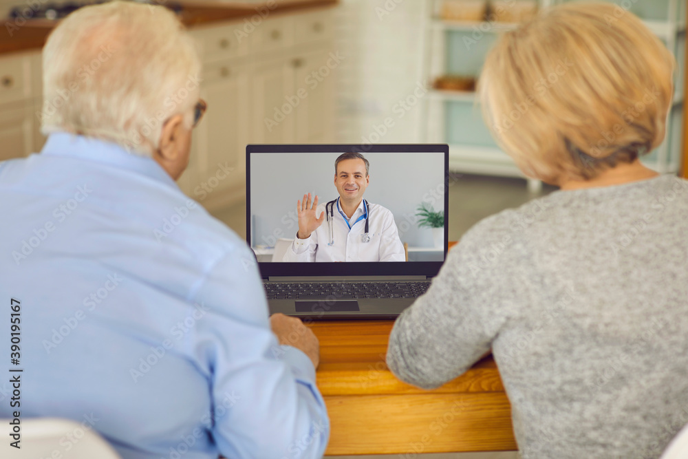 Obraz premium Back view of a senior couple sitting in front of a laptop and talking to a doctor online.
