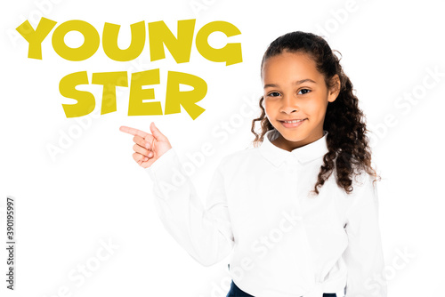 african american schoolgirl pointing with finger at youngster lettering while looking at camera isolated on white
