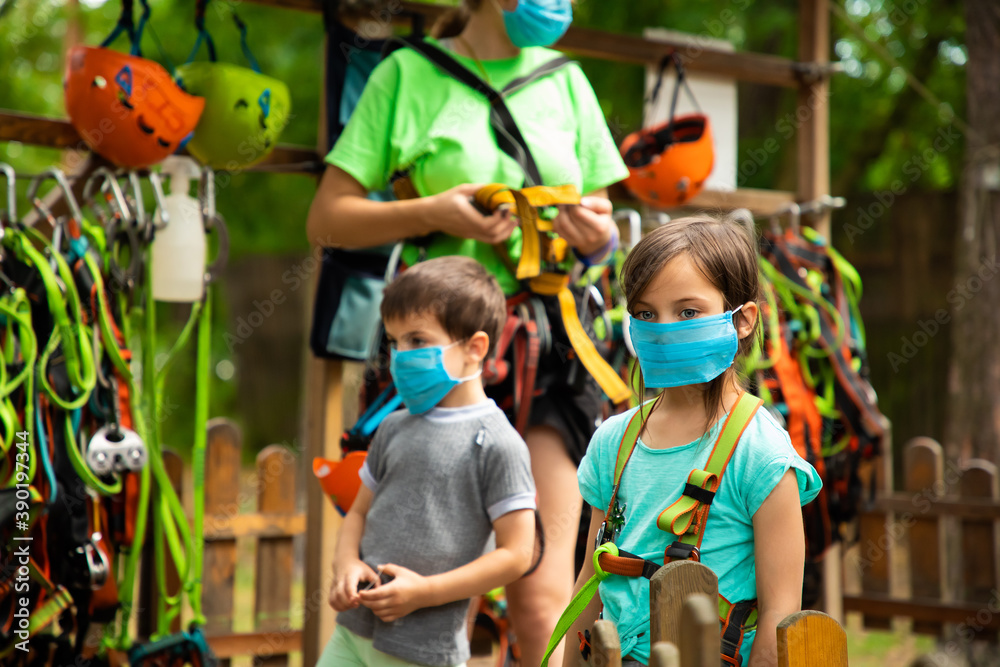 Little children in disposable masks standing in the equipping point in the sky rope park