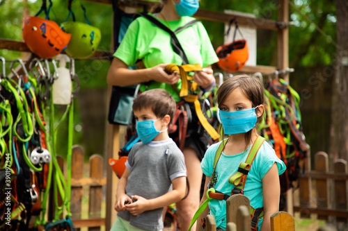 Little children in disposable masks standing in the equipping point in the sky rope park
