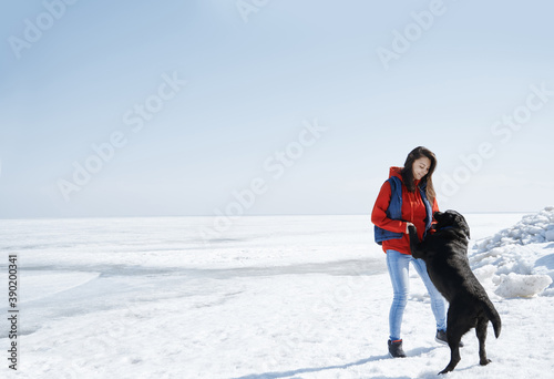 Young adult woman outdoors having fun with her black dog in icy landscape