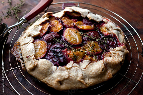 Close up of rustic plum crostata with lemon thyme on cooling rack