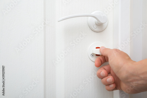 Young woman hand opening or closing lock of white toilet door. Closeup.