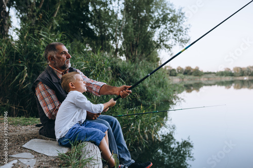 Картината върху платно boy fishing with his grandfather by the lake