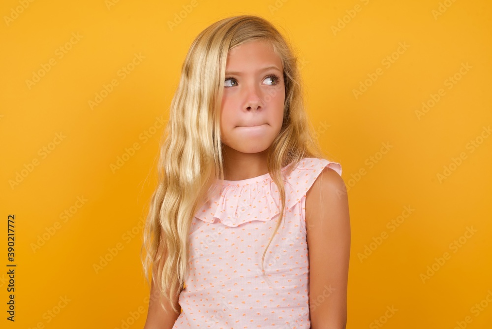 Amazed puzzled Beautiful Caucasian young girl standing against yellow background , curves lips and has worried look, sees something awful in front. Amazed puzzled Beautiful Caucasian young girl standing against yellow background , curves lips and has worried look, sees something awful in front.