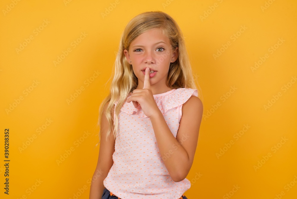Beautiful Caucasian young girl standing against yellow background makes hush gesture, asks be quiet. Don't tell my secret or not speak too loud, please! Beautiful Caucasian young girl standing against yellow background makes hush gesture, asks be quiet. Don't tell my secret or not speak too loud, please!