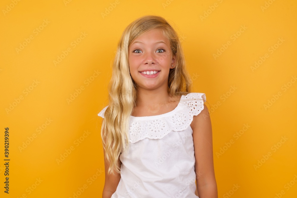 Beautiful Caucasian young girl standing against yellow background having broad white smile showing white teeth being excited to meet friends. Beautiful Caucasian young girl standing against yellow background having broad white smile showing white teeth being excited to meet friends.