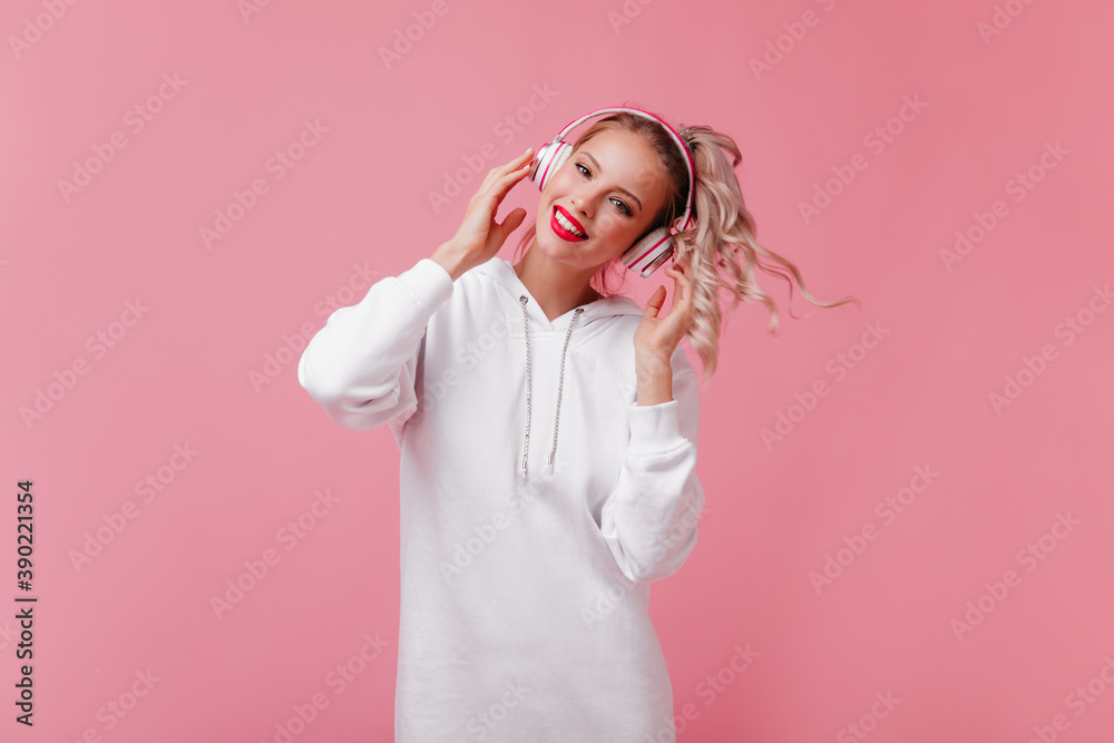 Portrait of pretty girl with curly ponytail in headphones on isolated background. Snow-white, friendly smile makes young model even more attractive Portrait of pretty girl with curly ponytail in headphones on isolated background. Snow-white, friendly smile makes young model even more attractive