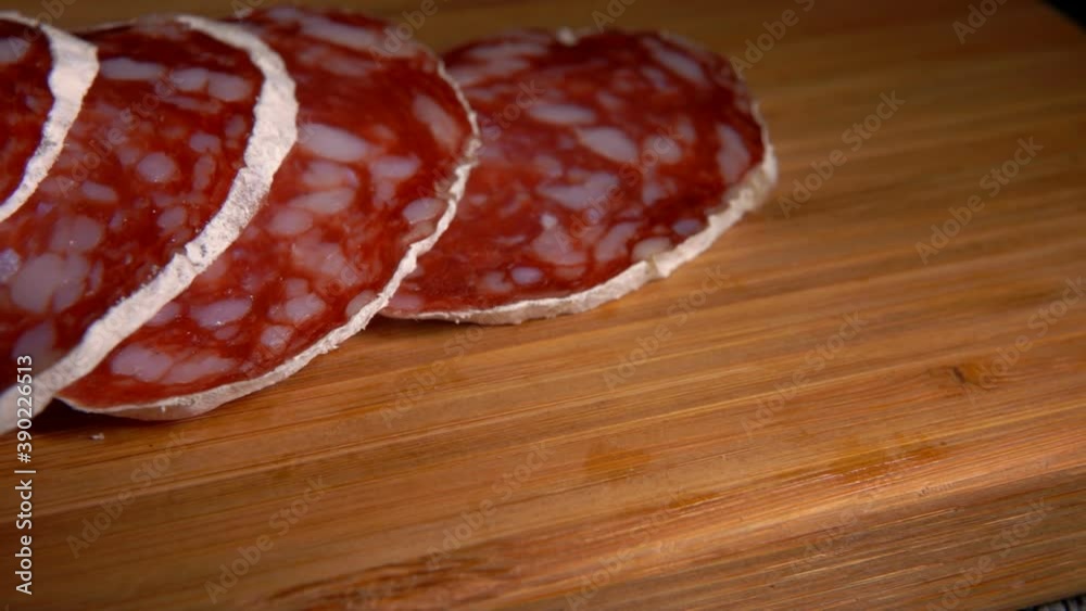 Close-up panorama of dry sausage in white skin taken from a wooden board with a fork on the background of pepper and greenery Close-up panorama of dry sausage in white skin taken from a wooden board with a fork on the background of pepper and greenery