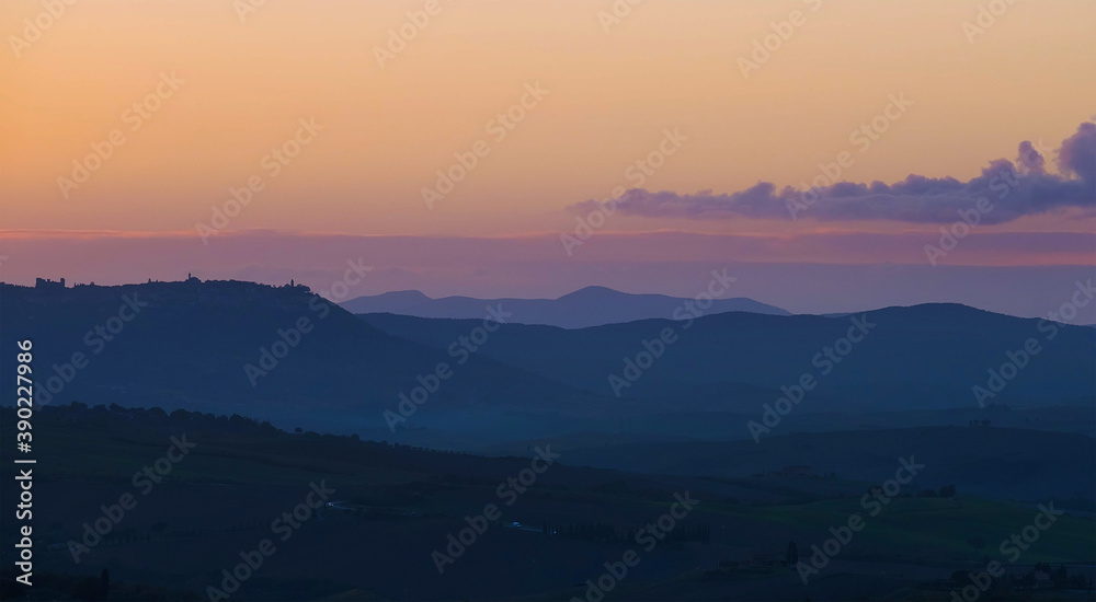 Early morning beautiful Tuscany hills  landscape view with plowed and green grass covered wavy fields. Sunrise light covering the meadows, fields and distant mountains.Pienza,province of Siena, Italy.