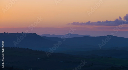 Early morning beautiful Tuscany hills landscape view with plowed and green grass covered wavy fields. Sunrise light covering the meadows, fields and distant mountains.Pienza,province of Siena, Italy.