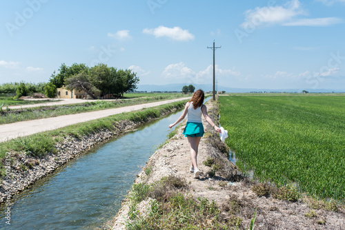 Young woman walking along the water channel in Delta del Ebro next to the rice fields. photo