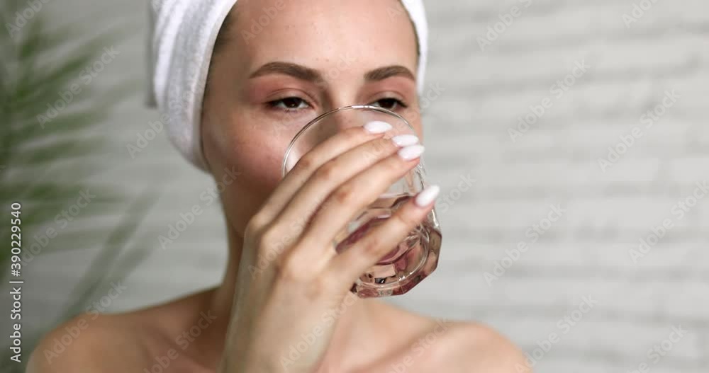 Attractive young brunette drinking water from glass while sitting at bathroom. Young woman with natural beauty maintaining body's water balance. Attractive young brunette drinking water from glass while sitting at bathroom. Young woman with natural beauty maintaining body's water balance.