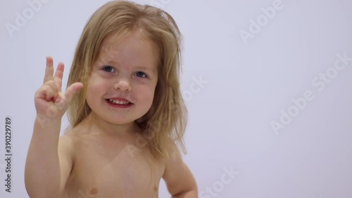 pretty little blonde girl laughing, showing 'one', 'two' and 'three' with her fingers shirtless on greyish background. Full HD footage