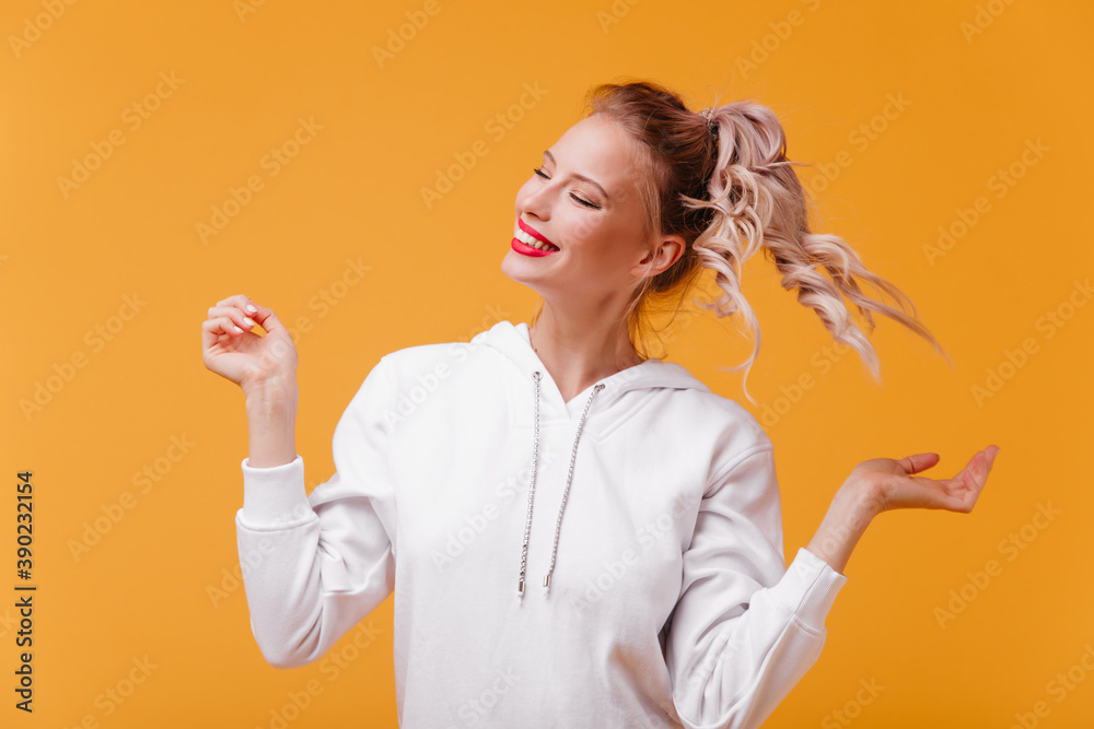 young woman in wonderful mood laughs with her eyes closed. Half-length portrait ofgirl with light-colored clothes with hood on bright isolated background young woman in wonderful mood laughs with her eyes closed. Half-length portrait ofgirl with light-colored clothes with hood on bright isolated background