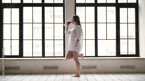 Young woman enjoys morning and music at home and drinks wine from a glass. Morning mood of a young woman on a day off