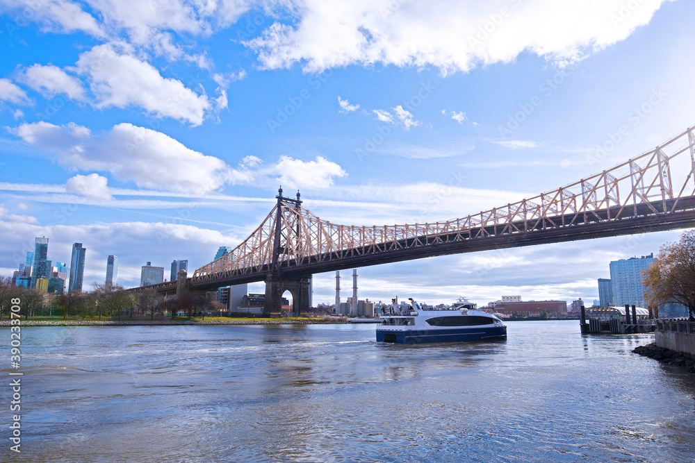Naklejka premium East River landscape in New York City near Roosevelt Island. Ferry motorboat brings passengers on island in early winter morning.