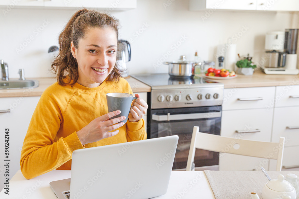 Mobile Office at home. Young woman sitting in kitchen at home working using on laptop computer. Lifestyle girl studying or working indoors. Freelance business quarantine concept. Mobile Office at home. Young woman sitting in kitchen at home working using on laptop computer. Lifestyle girl studying or working indoors. Freelance business quarantine concept.