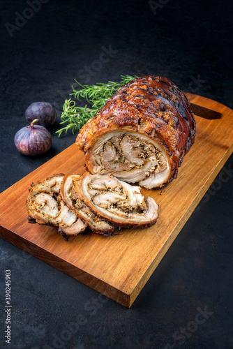 Traditional Italian Porchetta arrotolata pork meat sliced and as piece with herbs and figs offered as close-up on a modern design wooden board photo