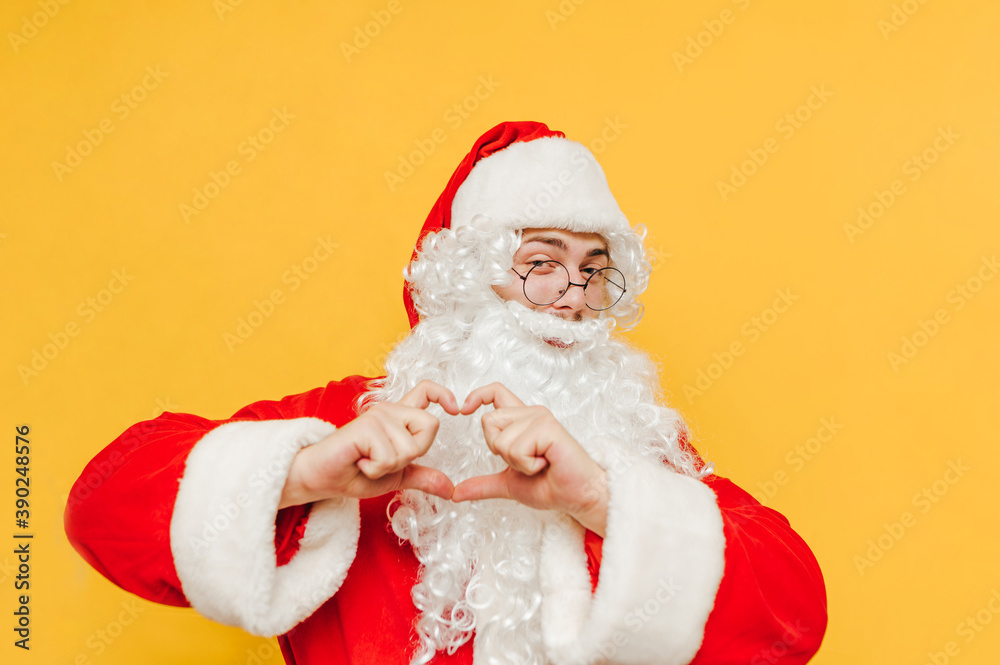 Positive Santa stands on a yellow background and shows his fingers a gesture of love with a smile on his face. Christmas concept. Positive Santa stands on a yellow background and shows his fingers a gesture of love with a smile on his face. Christmas concept.