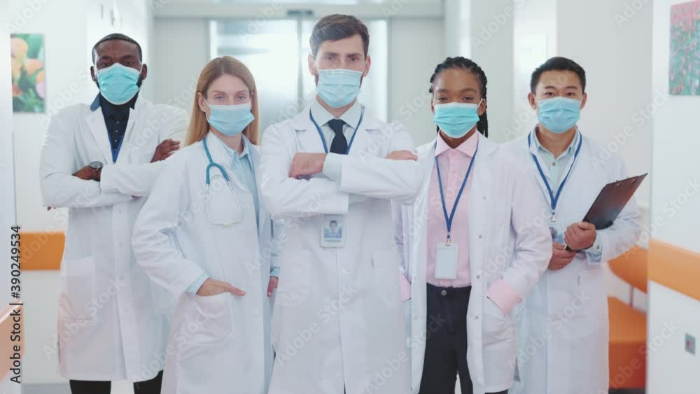 Portrait of five multi-ethnic doctors wearing face masks standing in corridor. Hospital staff of professional coworking medical workers and asistants. Portrait of five multi-ethnic doctors wearing face masks standing in corridor. Hospital staff of professional coworking medical workers and asistants.