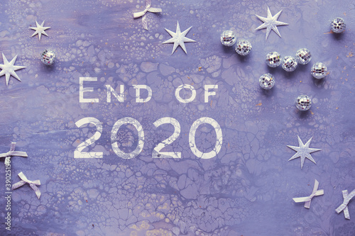 Text End of 2020. Flat lay on acrylic painted board with mirror balls, silver stars and bows.