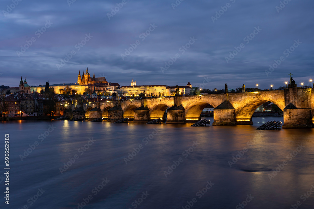 
Charles Bridge on the Vltava river and statues on it and lit street lights and light from lamps at night in the center of Prague in the Czech Republic and there are clouds in the sky