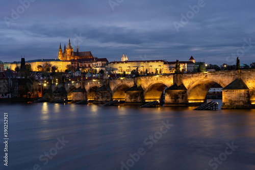 
Charles Bridge on the Vltava river and statues on it and lit street lights and light from lamps at night in the center of Prague in the Czech Republic and there are clouds in the sky