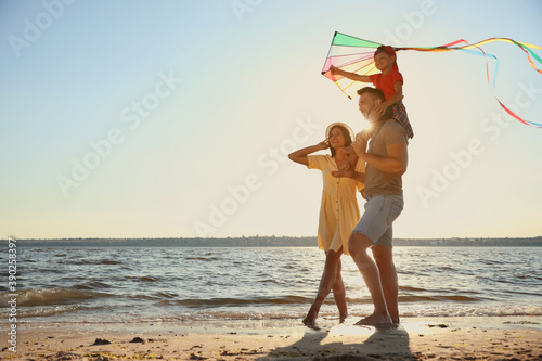 Happy parents and their child playing with kite on beach near sea. Spending time in nature