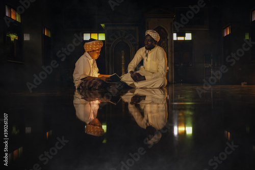 muslim boy sitting in mosque with islamic teacher learning koran book