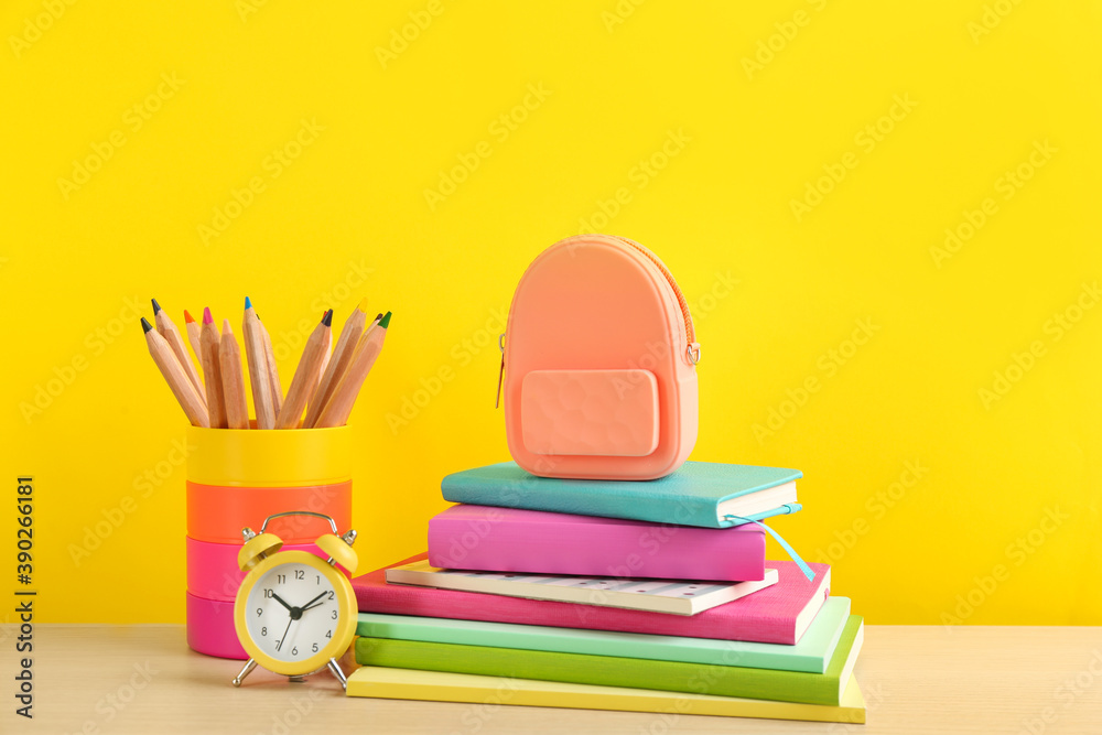 Different school stationery and alarm clock on table against yellow background. Back to school