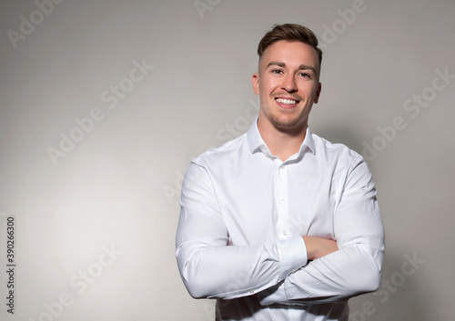 Handsome young man posing on grey background in white dress shirt while smiling