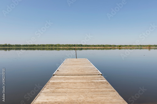 A Wood Pier Juts over a Still Lake with a Treeline in the Background