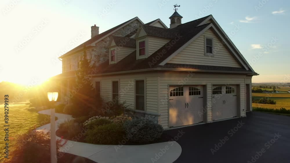 Dramatic sunrise illuminates large stone farm house with green front yard. Morning, wake up, new beginning theme. Aerial truck shot.