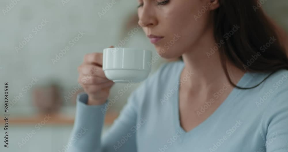 Tracking shot of melancholic young woman drinking tea, holding cup with hot drink, suffering from depression Tracking shot of melancholic young woman drinking tea, holding cup with hot drink, suffering from depression