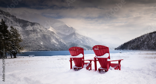 A pair of wooden chairs overlooking Waterton Lakes National Park Canada during the winter with a glacier lake colours.