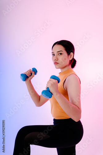 Healthy asian woman with two dumbbells on pastel background.